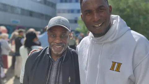 Jon Wright/BBC Clem Turner and Isaac Turay stand outside and smile at the camera. There is a crowd in the background.
