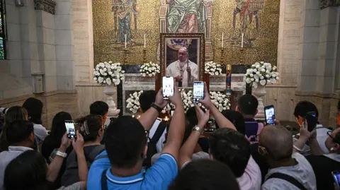 Getty Images People take photos of an altar with Pope Francis' photo at the Manila Cathedral in the Philippines