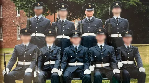 Neil Ferriby Neil Ferriby is standing among nine RAF personnel for an official photograph. He is wearing ceremonial RAF uniform with a blue peaked hat, blue jacket with white belt, shirt and tie. He and his colleagues are all carrying guns with bayonets.