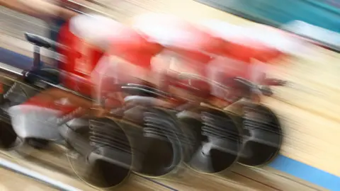 A very blurred image of four cyclists racing in a velodrome.