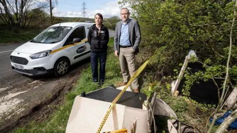 Durham County Council Cllr Mark Wilkes, Durham County Council’s Cabinet member for neighbourhoods and climate change, is pictured with neighbourhood warden Claire Liddle looking at a fly-tip in the Esh area with a Durham County Council van behind them 