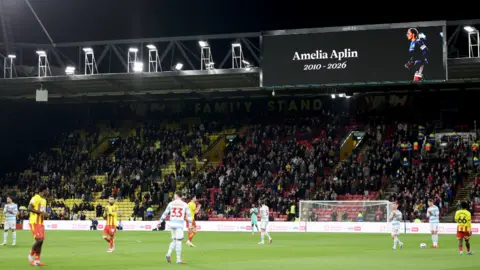PA Media Players from both teams and fans stand and applaud in the 15th minute of the match in memory of 15-year-old Oxford United academy goalkeeper Amelia Aplin, who died last week during the Sky Bet Championship match at Vicarage Road, Watford.