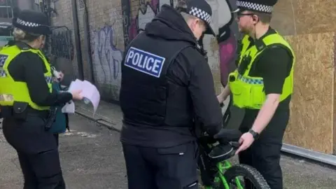 South Yorkshire Police Three police officers are stood in a street with an e-bike