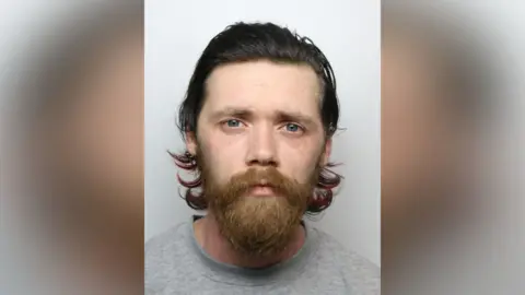 A police mugshot of Joshua Rothery, who has long dark hair and a ginger beard.