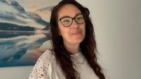 Rachel Murphy has long dark hair. She is wearing a cream top and glasses.