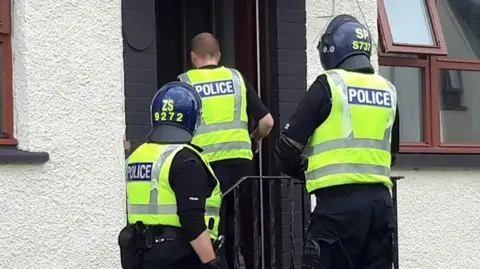 A stock picture supplied by Police Scotland showing three officers in protective gear entering a home address