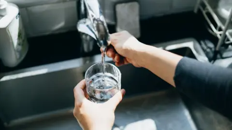 The hand of an unseen person filling a glass with water from a kitchen tap.