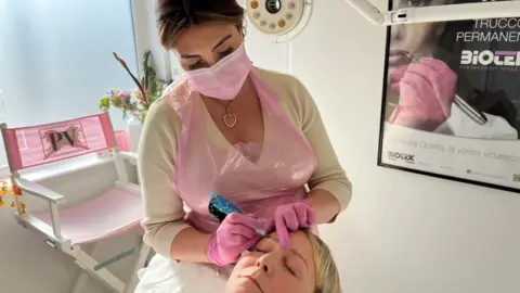 Shaun Whitmore/BBC Polly Vincent giving an eyebrow tattoo