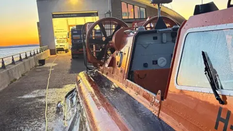 A stock image showing the side of a lifeboat, looking towards the RNLI equipment unit with the sea and setting sun in the distance.