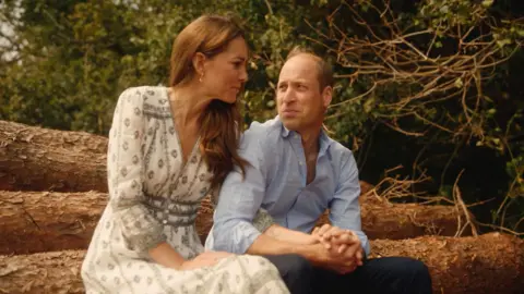 Will Warr/Kensington Palace The Prince and Princess of Wales sit together holding hands. They gaze at each other adoringly