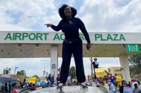 Reuters A demonstrator stands atop a vehicle and shouts slogans as others carry banners while blocking a road leading to the airport, during a protest over alleged police brutality, in Lagos, Nigeria October 12, 2020.