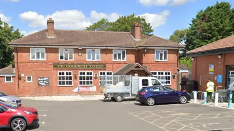 Google A pub car park with a large building with the words The Goodrest Tavern in gold lettering on a green sign