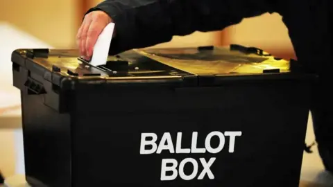 PA Media A black box has white letters saying Ballot Box and a hand is putting in a folded ballot paper into it