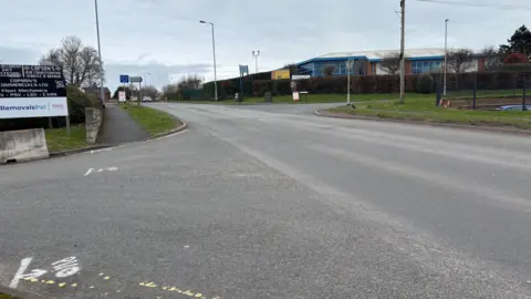 A wide road featuring road markings and lamposts in the background.