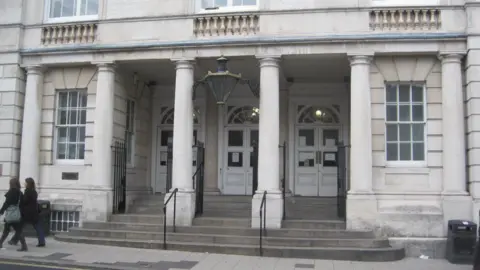 PA Media The exterior of Lewes Crown Court. A light grey, stone building with three large white doors. Two people walk right to left on the pavement in front of the building