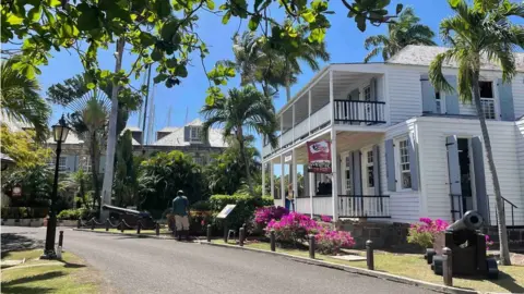 A picture from the area shows a white building, a cannon, lush green foliage and blue skies
