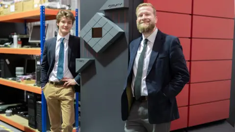 RWB Auctions Two men in suits smile at the camera while standing either side of one of the huge units, taller than themselves. The unit is black and red.