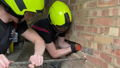 Dunstable Community Fire Station  Two firefighters removing bricks from a wall