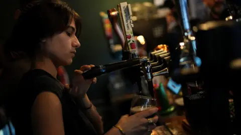 Reuters A female asian bartender in her twenties pulling a pint from some pumps in a bar.
