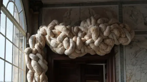 Nicola Turner Large knotted woollen shapes above a door frame in a house. The walls are marbled.