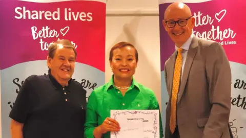 Oxfordshire County Council Roger and Kym Garnett stood holding a certificate, next to Martin Reeves.