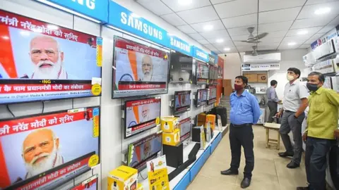 Getty Images People watch a live telecast of Prime Minister Narendra Modi's address to the nation, at Khanna Market, on October 20, 2020 in New Delhi, India.