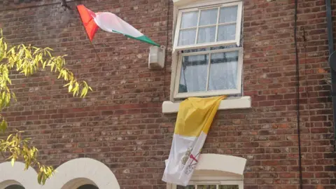 Paul Burnell/BBC A red, white and green Italian flag and a yellow and white Vatican flag with the HOly See's coat of arms fly from a house in Little Italy, Ancoats, Manchester.