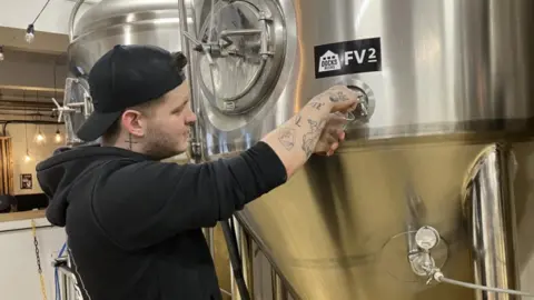 Lara King / BBC Elliot Reynolds pouring a pint from a fermentation vessel at a brewery