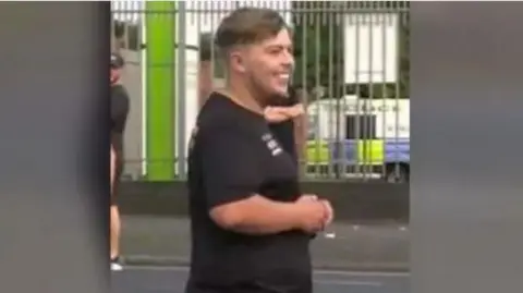 GMP Smith stands in the street smiling wears a a black T-shirt