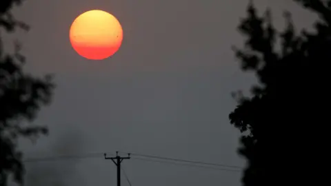 Jamie Cooper Um pôr do sol vermelho vivo. Um poste e uma linha de telégrafo podem ser vistos em primeiro plano.