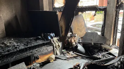 The room badly damaged by fire. The window is smashed through and the furniture is severely burned 