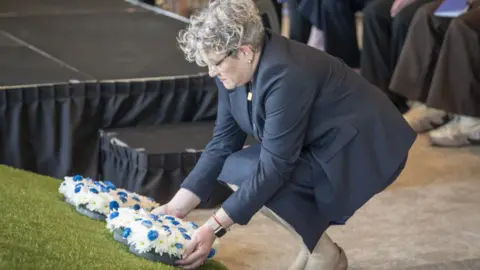 PA Media Ashley Dalton, wearing a dark blue suit, kneels as she lays a wreath during a ceremony marking the fifth anniversary of the Covid-19 pandemic 