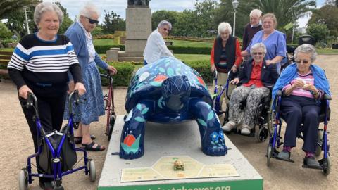 Care home residents standing next to tortoise sculpture