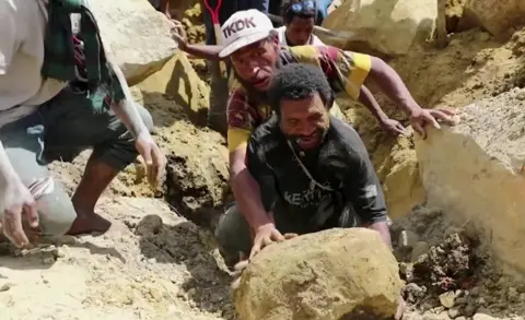 Two men struggling to move a boulder