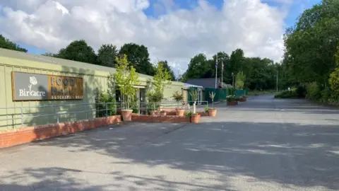 The Birkacre Garden Centre, Chorley, on a sunny day showing the car park and the food hall with the entrance surrounded by plants