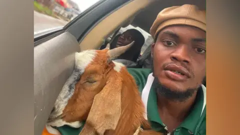 Promise Okoro poses for a selfie in a car with his goat.