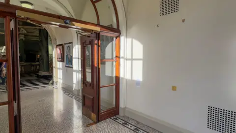 PA Media A hallway with double wooden doors, there is a large empty space on the wall where the portrait hung before it was damaged.