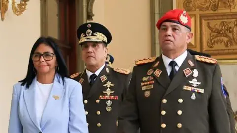 Handout via REUTERS Venezuela's acting President Delcy Rodríguez walks with Gen Gustavo González López in Caracas, Venezuela, on 19 March. She is wearing a light blue jacket and white shirt, while Lopez is wearing military uniform, including a red beret.