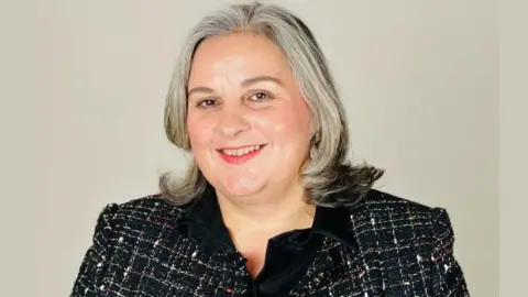 Somerset NHS Foundation Trust a portrait photo of a smiling woman in a smart jacket against a grey background