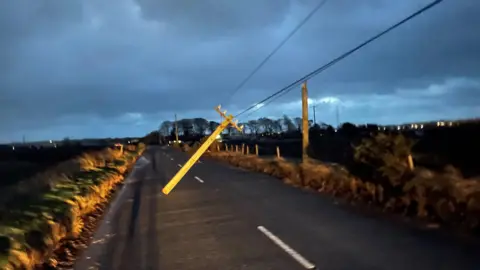 PA Media A telegraph pole hanging by electric lines across Blaris Road in County Antrim 