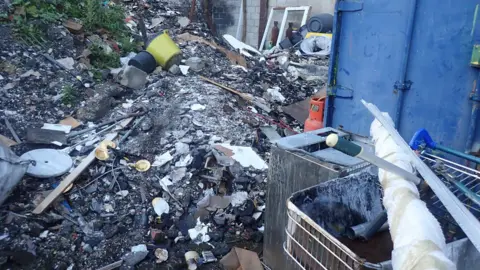 A huge pile of rubbish including ash, buckets and a shopping trolley