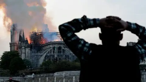 AFP via Getty Images A man watches the landmark Notre-Dame Cathedral burn, engulfed in flames, in central Paris on April 15, 2019