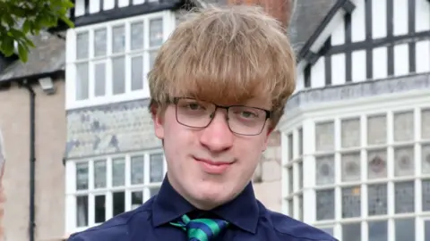 A man with short brown hair and glasses wearing a blue shirt