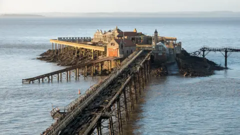 Getty Images Birnbeck Pier in Weston-super-Mare. The pier is damaged and in disrepair, with a heavily damaged wooden walkway and dilapidated buildings.