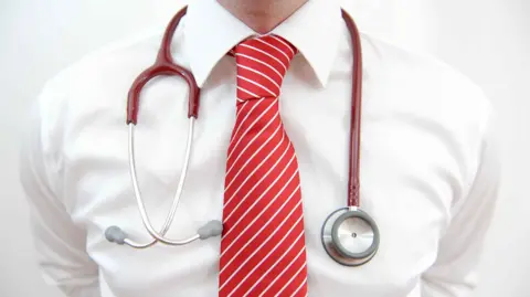 The upper torso of a doctor wearing a white shirt with red tie and a stethoscope around their neck
