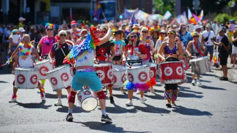 PA Media A crowd of drummers leading a parade at Bristol Pride 2025. Many of them have rainbow clothing, accessories and flags.