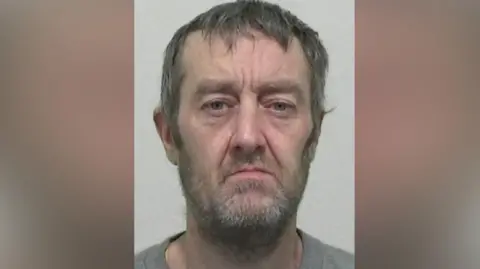 Mugshot of Robinson. He has a scruffy grey beard and messy greying hair.