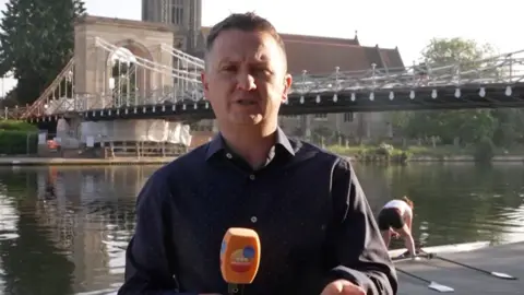 Weather presenter Matt Taylor reporting near a river and bridge