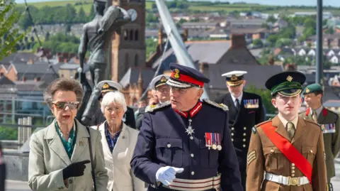 A groups of people, some in naval uniform, walk across Derry's Ebrington Square. Two of the people are women, in the company of five uniformed men