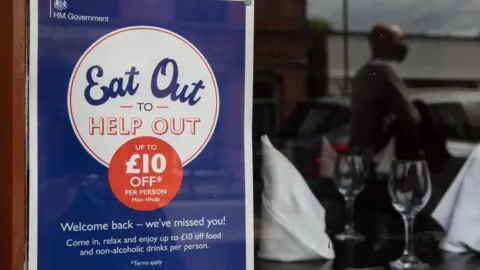 Getty Images An Eat Out to Help Out poster in a window with two wine glasses and a blurred reflection of a customer